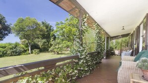 A covered patio with a view of a garden, a wooden railing, and outdoor furniture. - Villa Monserrato with garden and sea view (Porto Azzurro)
