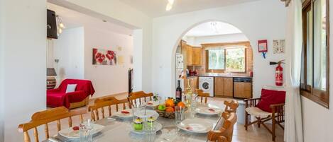 Un comedor con una mesa redonda dispuesta para cuatro, una cocina al fondo y un sofá rojo en la sala.