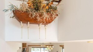 En rummelig opholdsstue med en rød sofa, et maleri af røde blomster og en træhylde med blomsterarrangement.