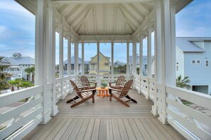 Une terrasse en bois couverte, dotée de rampes blanches, de deux fauteuils Adirondack en bois et d’une petite table ronde avec une seule chaise.