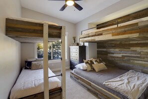 Relax in this cozy retreat with a loft-style bed, lower bunk bed, and single bed, plus a dresser and table with a vase of flowers.