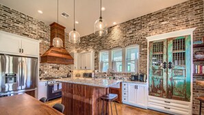 A kitchen with a rustic brick wall, stainless steel appliances, and a wooden island with stools. - River Repose Rr 7134 4 Bedroom Home by RedAwning (New Braunfels)
