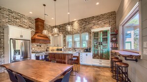 A modern kitchen with a brick wall, stainless steel appliances, and a wooden dining table. - River Repose Rr 7134 4 Bedroom Home by RedAwning (New Braunfels)
