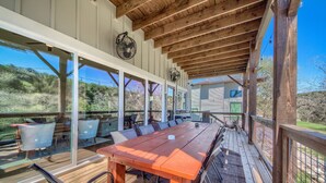 An outdoor dining area with a long wooden table and chairs, surrounded by glass walls and wooden beams. - River Repose Rr 7134 4 Bedroom Home by RedAwning (New Braunfels)
