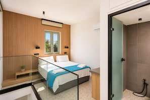 Ein modernes Schlafzimmer mit Bett, Nachttischen, einem Fenster und einer Duschgelegenheit.