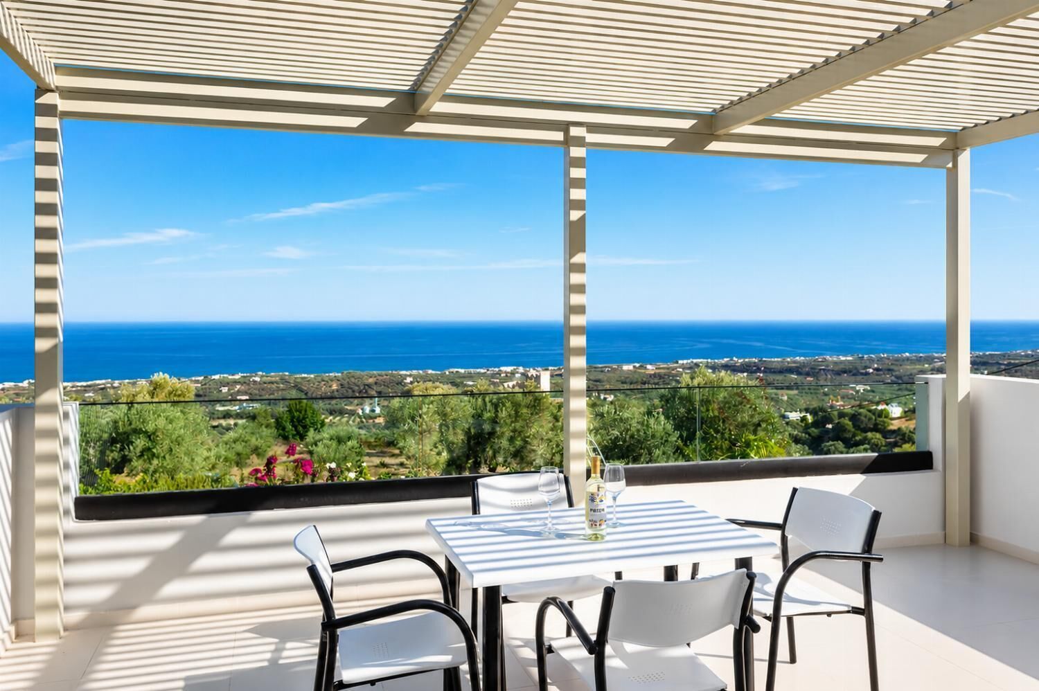 A balcony with a table and chairs, overlooking a coastal landscape.