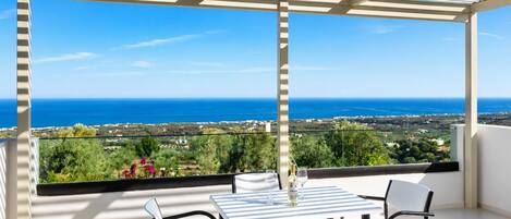 A balcony with a table and chairs, overlooking a coastal landscape.