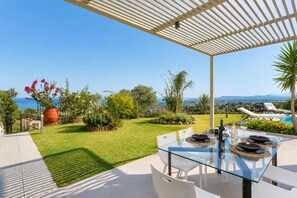 An outdoor patio with a glass table, white chairs, and a view of the sea.