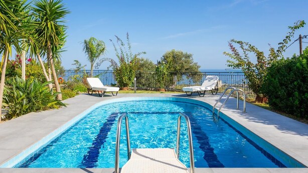 En pool med två solstolar, omgiven av tropiska växter och med en fri utsikt över havet.