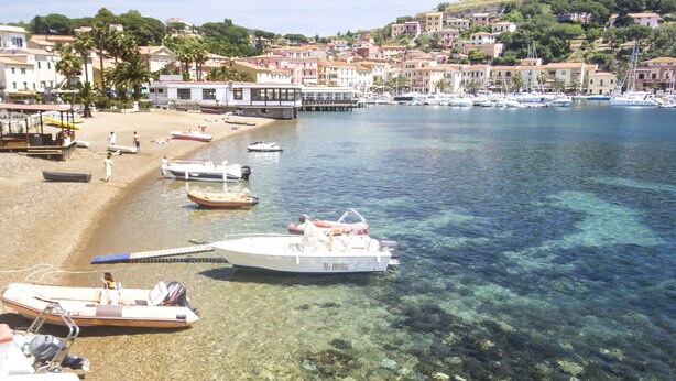 Un borgo costiero con acque cristalline, barche ormeggiate sulla riva e palazzi con balconi affacciati sul mare.