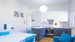 Una cucina compatta con mobili bianchi, forno integrato e lampada a sospensione.