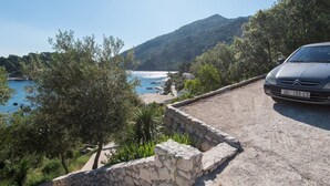 A stone wall leading to a coastal road with a parked car. - House DANIVA located in front of the sea (Okuklje)