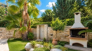 Un jardín con muro de piedra, una palmera y un horno de ladrillo al aire libre.