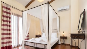 Una cama con dosel con sábanas blancas, suelo de madera, mesita de noche con lámpara y aire acondicionado instalado en la pared.