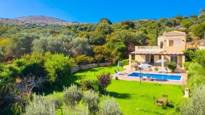 Una casa de dos pisos con piscina, rodeada de vegetación exuberante y colinas.