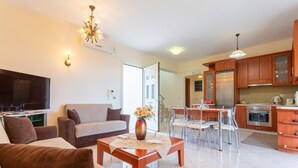 Una sala de estar moderna con sofá, mesa de centro y televisor. La cocina tiene armarios de madera y un comedor con sillas.