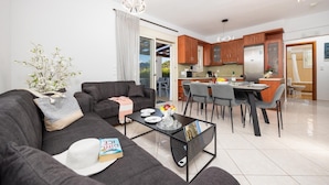 A modern living room with a sofa, coffee table, and dining area. - Villa Georgia - Three Bedroom Villa, Sleeps 6 (Crete)