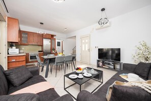 Ein modernes Wohnzimmer mit Sofa, Couchtisch und Fernseher. Es gibt eine Küchenzeile mit Schränken und Geräten.