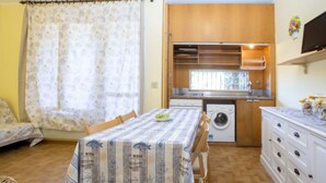 Una cocina compacta con lavadora, una mesa de comedor con mantel estampado de peces y un mueble pequeño con frascos.
