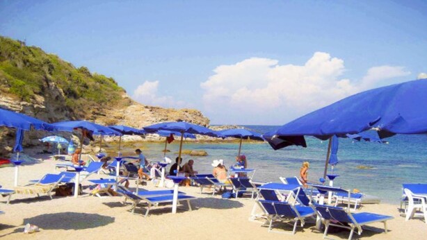 Una playa con sombrillas azules y tumbonas.