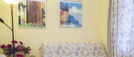 A room with a patterned sofa, a lamp, and two National Parks Centennial posters.