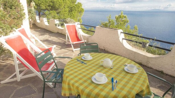 Une terrasse extérieure avec une table dressée pour deux personnes, des chaises et une vue sur la mer.