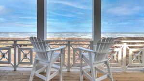 A covered deck with two white Adirondack chairs facing a beach view. - 8-bedroom home w/ Gulf-Front Views + Amenities (Port Aransas)
