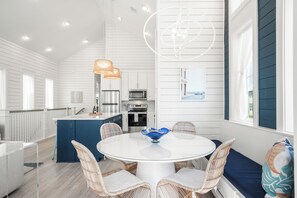 Una cocina moderna con armarios blancos, una isla azul y una mesa redonda con sillas de mimbre.