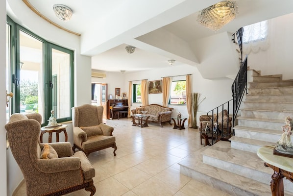 A spacious living room with a piano, a sofa set, and a staircase leading to an upper floor.