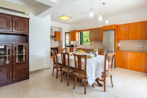 A modern kitchen with wooden cabinets, a dining table set for six, and a refrigerator.