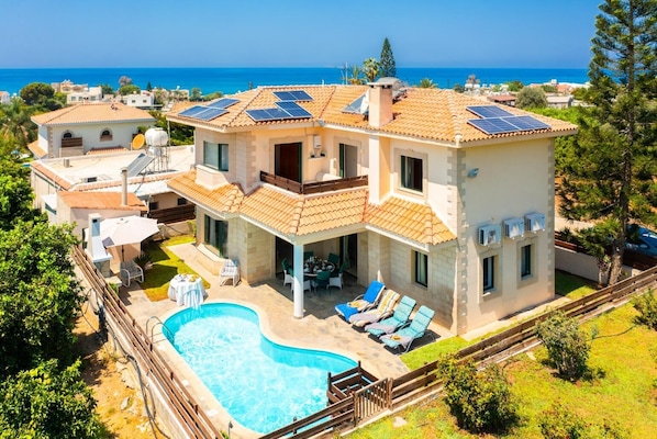 Une maison à deux étages avec une piscine, des panneaux solaires et une vue sur la mer.