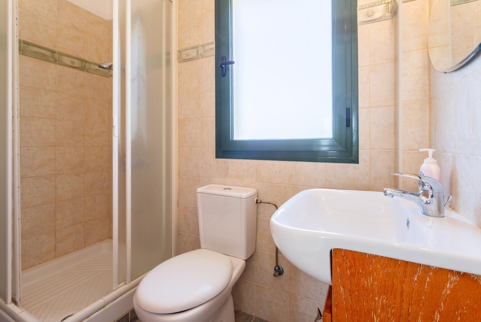 Un baño con ducha, inodoro, lavamanos y una ventana sobre el lavamanos.