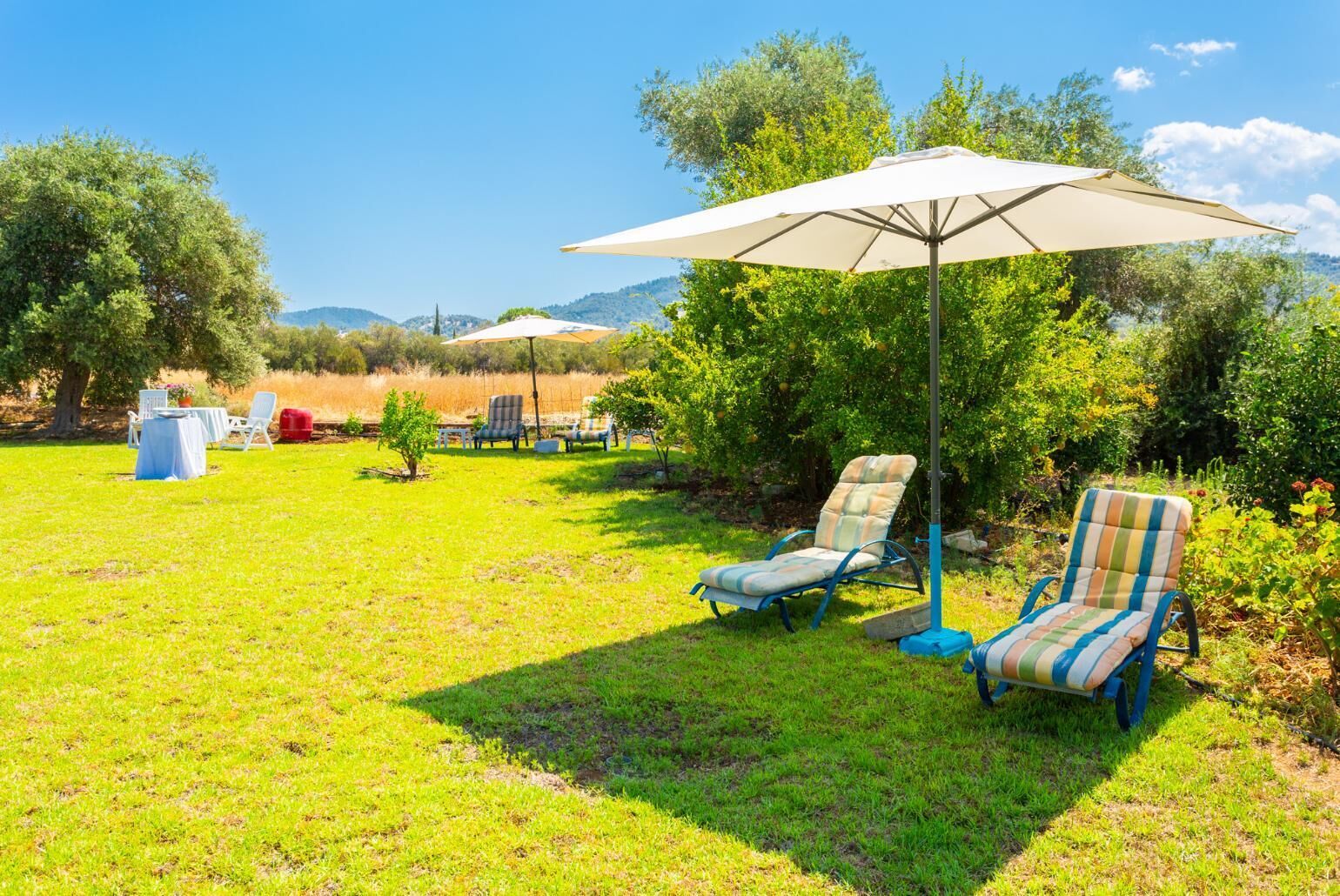 Un espacio al aire libre con césped, dos sillones de descanso y una mesa bajo un gran paraguas.