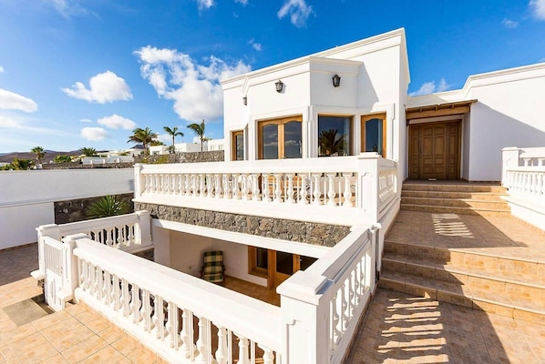 A two-story building with a balcony, stone wall, and a wooden door.