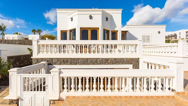 Un edificio blanco con fachada de piedra, varios balcones y un patio con tejas.
