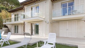 A two-story building with a balcony and a covered outdoor seating area with white lounge chairs.