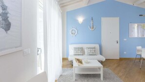 A room with a blue wall, a white door, a white sofa with patterned cushions, a white coffee table, and nautical-themed wall decor.