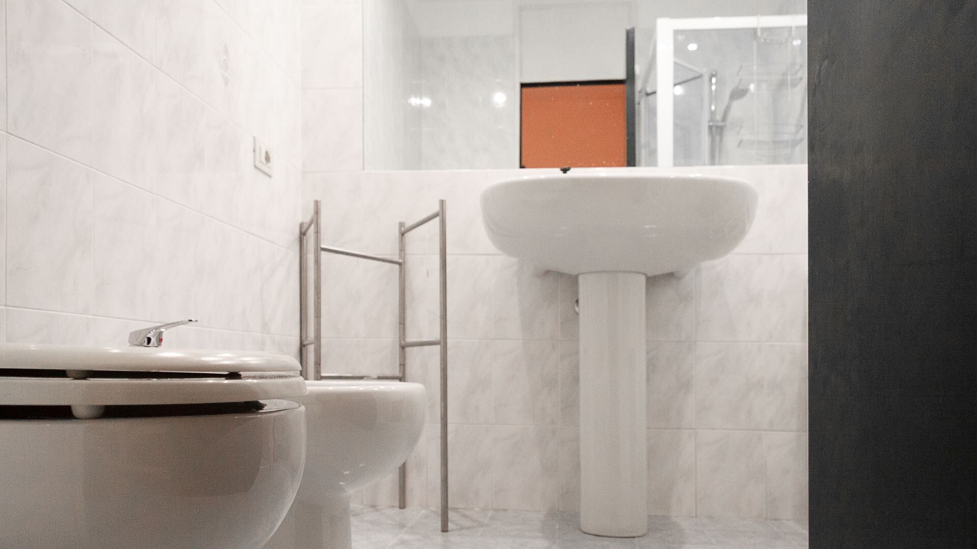 A modern bathroom with white marble tiles, a central sink, and two toilets.