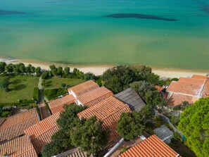 Enjoy a serene beachfront view from this coastal property with lush greenery and terraced roofs.