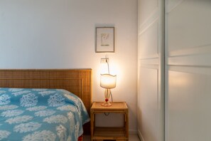 Un lit recouvert d’une couvre-lit à motifs bleus, une table de chevet avec une lampe et un tableau encadré au mur.