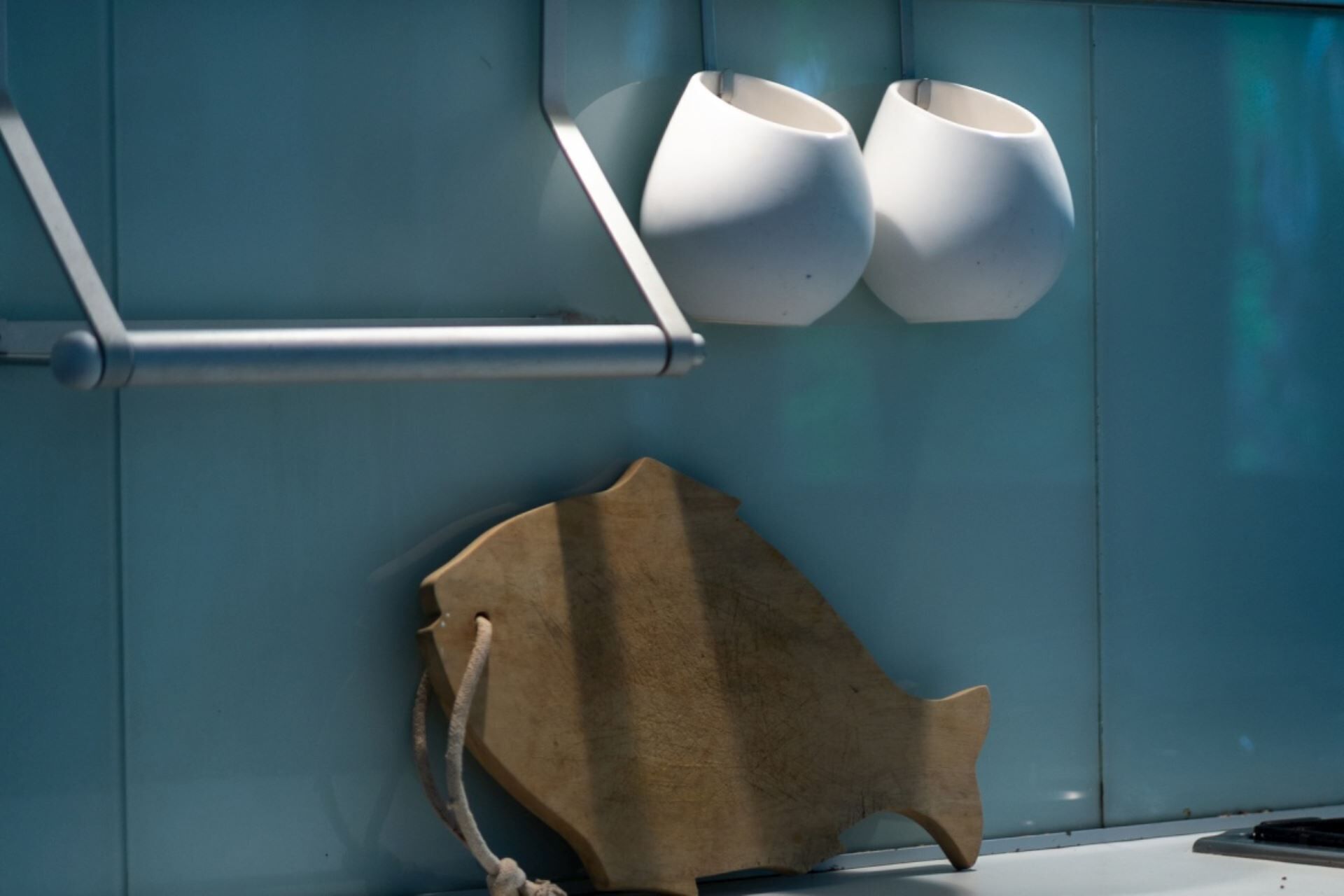 Pareda com três vasos de cerâmica branca e um objeto em forma de peixe de madeira.