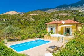 A villa with a swimming pool, surrounded by lush greenery and mountains.