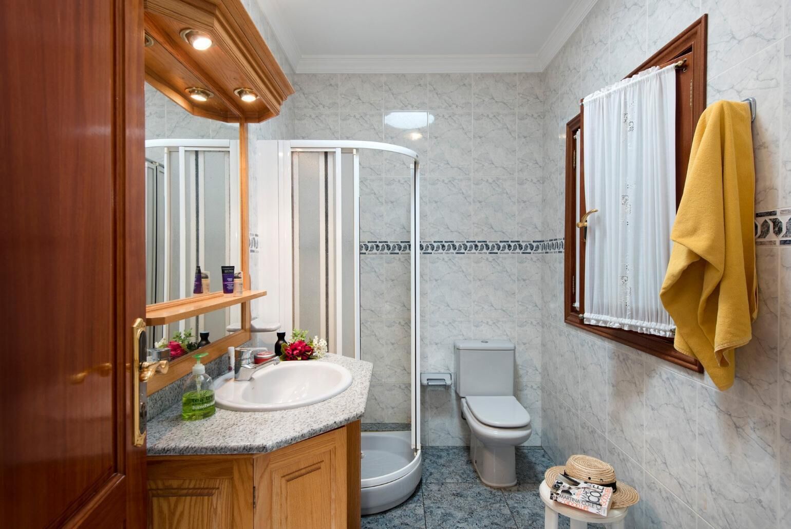 A bathroom with a wooden vanity, a white sink, a mirror, a shower enclosure, a toilet, and a towel rack.