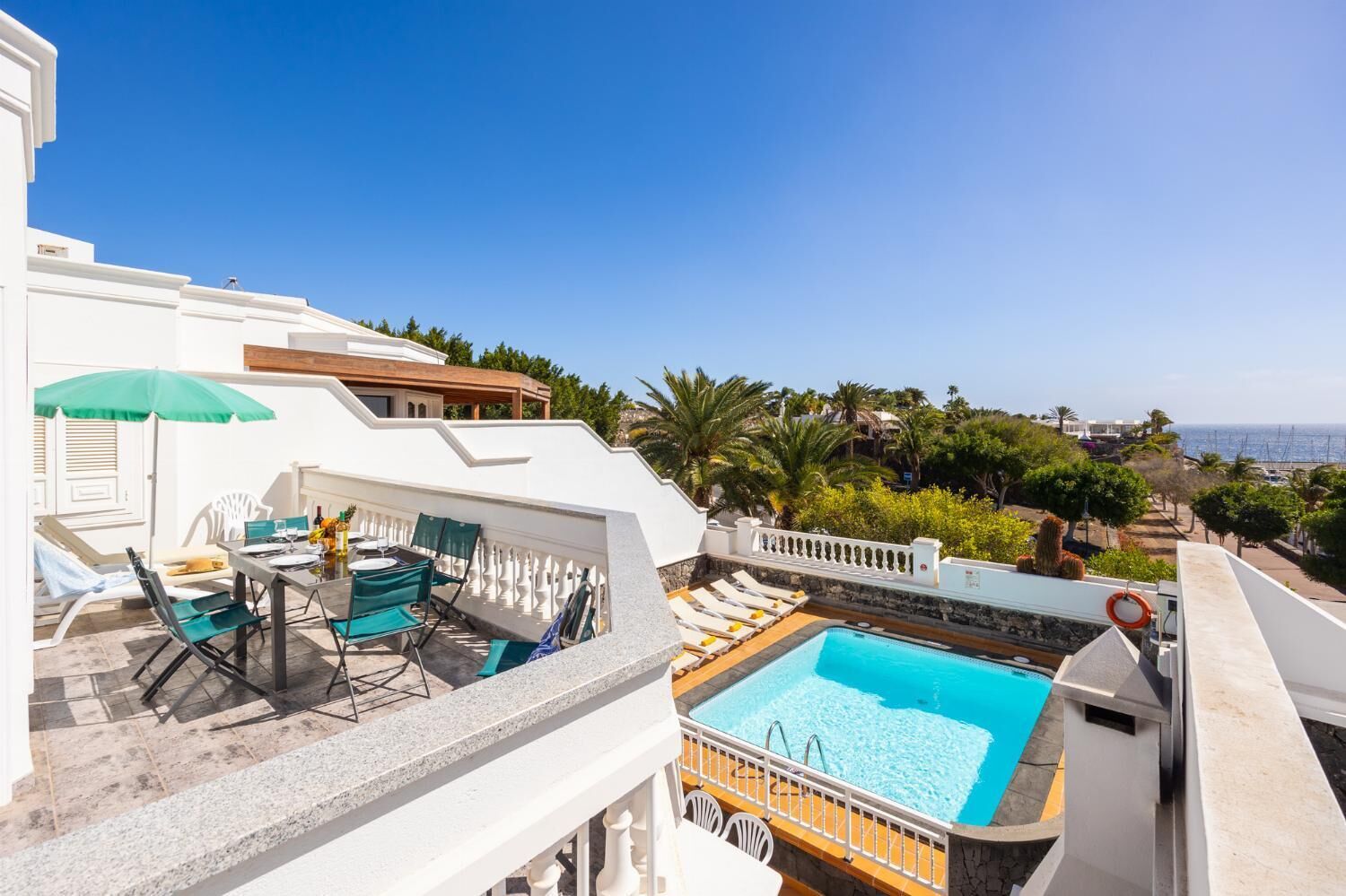 Un área de piscina en la azotea con sillones de descanso y una mesa, con vistas a un paisaje pintoresco y el mar.
