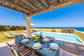 Un espace repas aménagé au bord de la piscine, avec une table dressée pour quatre personnes, offrant une vue sur la piscine et la mer.