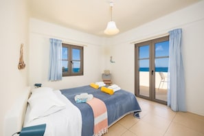 Une chambre à coucher avec un lit, une fenêtre, une porte donnant sur un balcon et un luminaire suspendu.