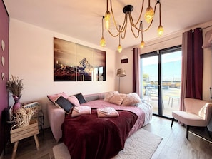 A modern bedroom with a large bed, a view of the outdoors, and a chandelier.