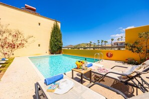 Zona de piscina con sillones, una mesa con bebidas y vista al mar.