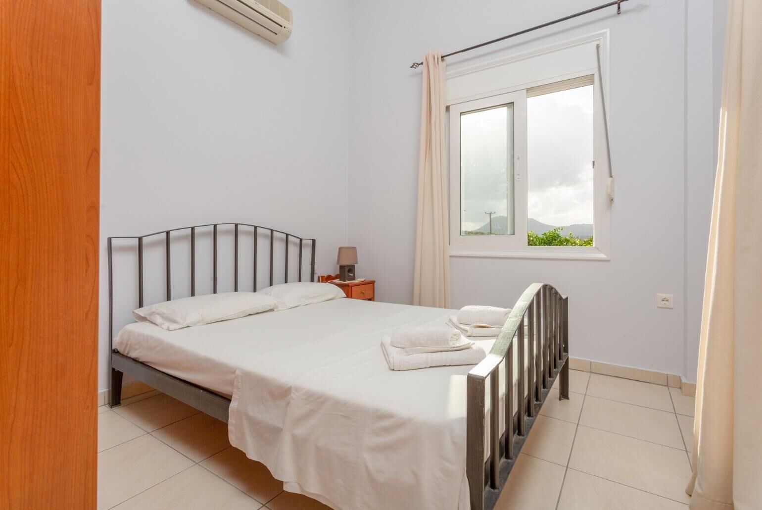 Une chambre à coucher avec un lit, une table de chevet, une fenêtre avec des rideaux et une vue sur la verdure à l’extérieur.