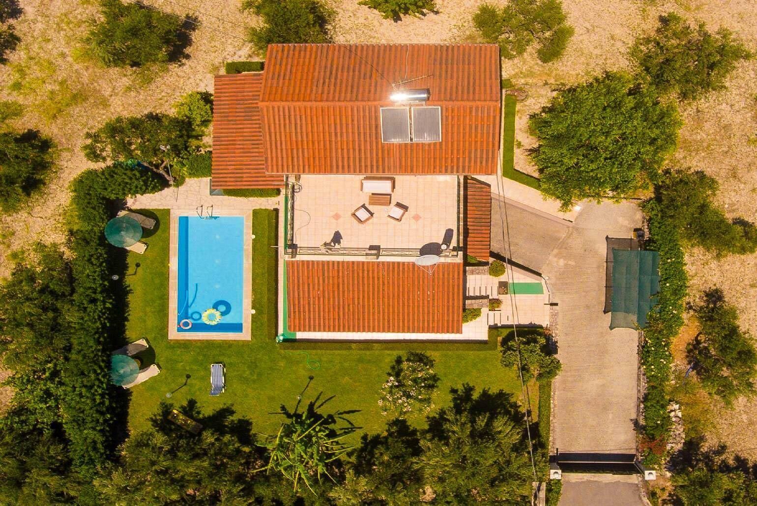 Luchtbeeld van een huis met een zwembad, een terras met zitplaatsen en een omheinde tuin.